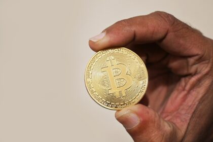 Mão segurando uma moeda física representando o Bitcoin